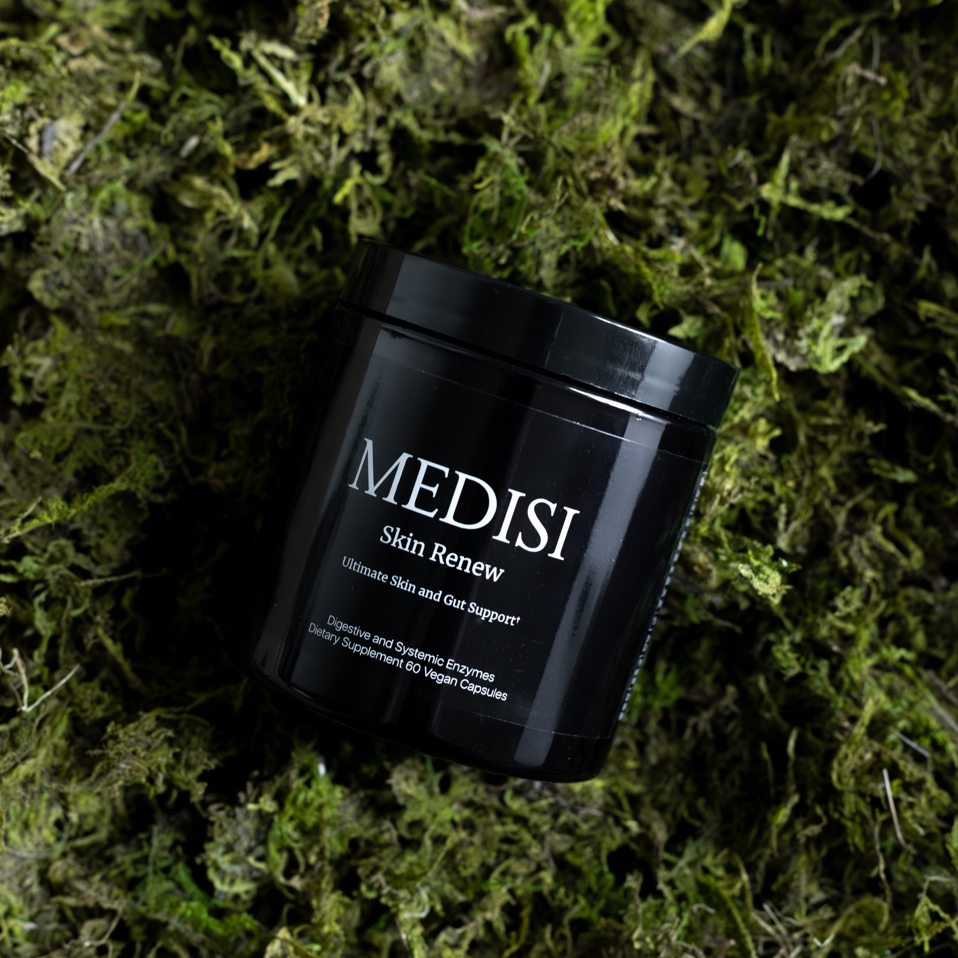 Angled view of Medisi Skin Renew jar showing white label text on a black jar resting on green moss